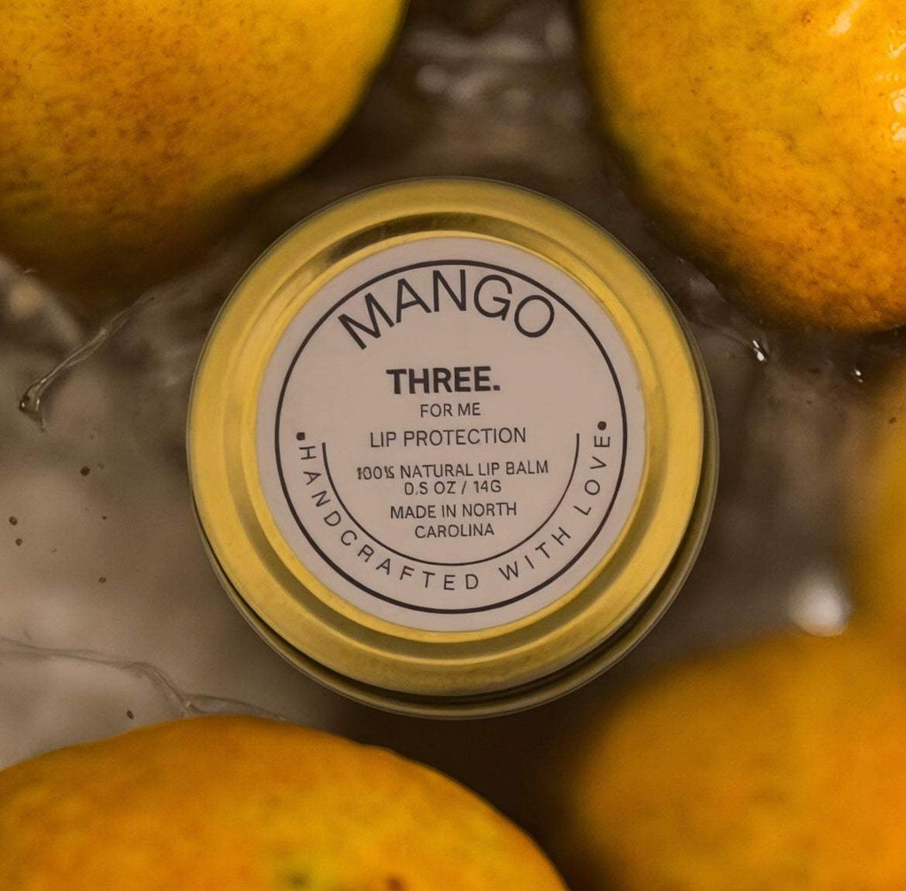 THREE. Mango Lip Protection coconut-free natural lip balm tube with mango and natural ingredients background